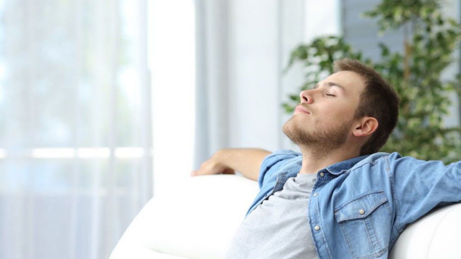 Symbolbild für angenehmes Raumklima: EIn Mann entspannt im Sofa und fühlt sich sichtlich wohl im Wohnraum.