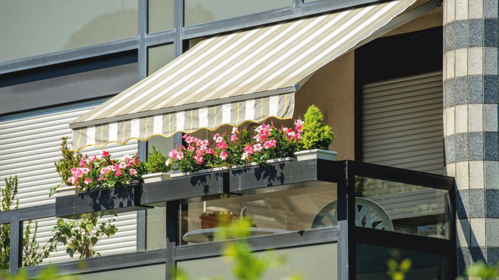 Mit Markise beschatteter Balkon und Fenster mit geschlossenen Rolläden