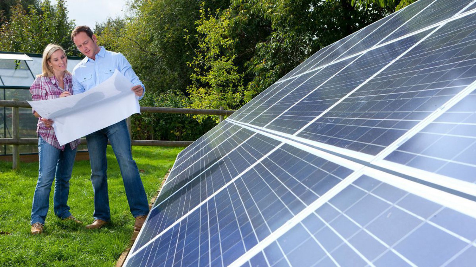 ein Paar steht mit einem Bauplan vor einer PV-Anlage