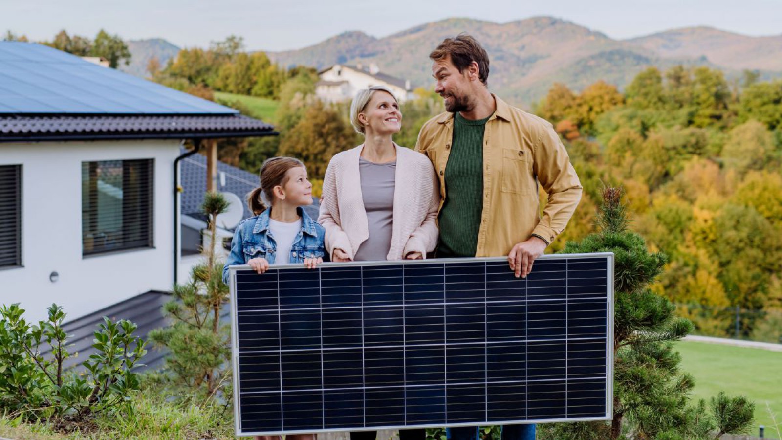 Eine Familie steht vor ihrem Haus und h&auml;lt ein PV-Paneel.
