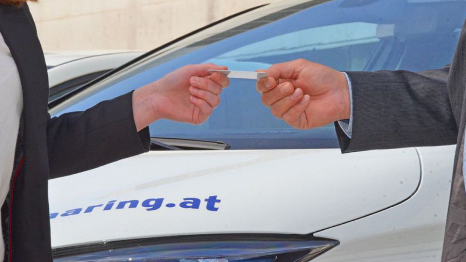 Eine Person übergibt eine Zugangskarte für ein Carsharing-Elektroauto an eine andere Person.