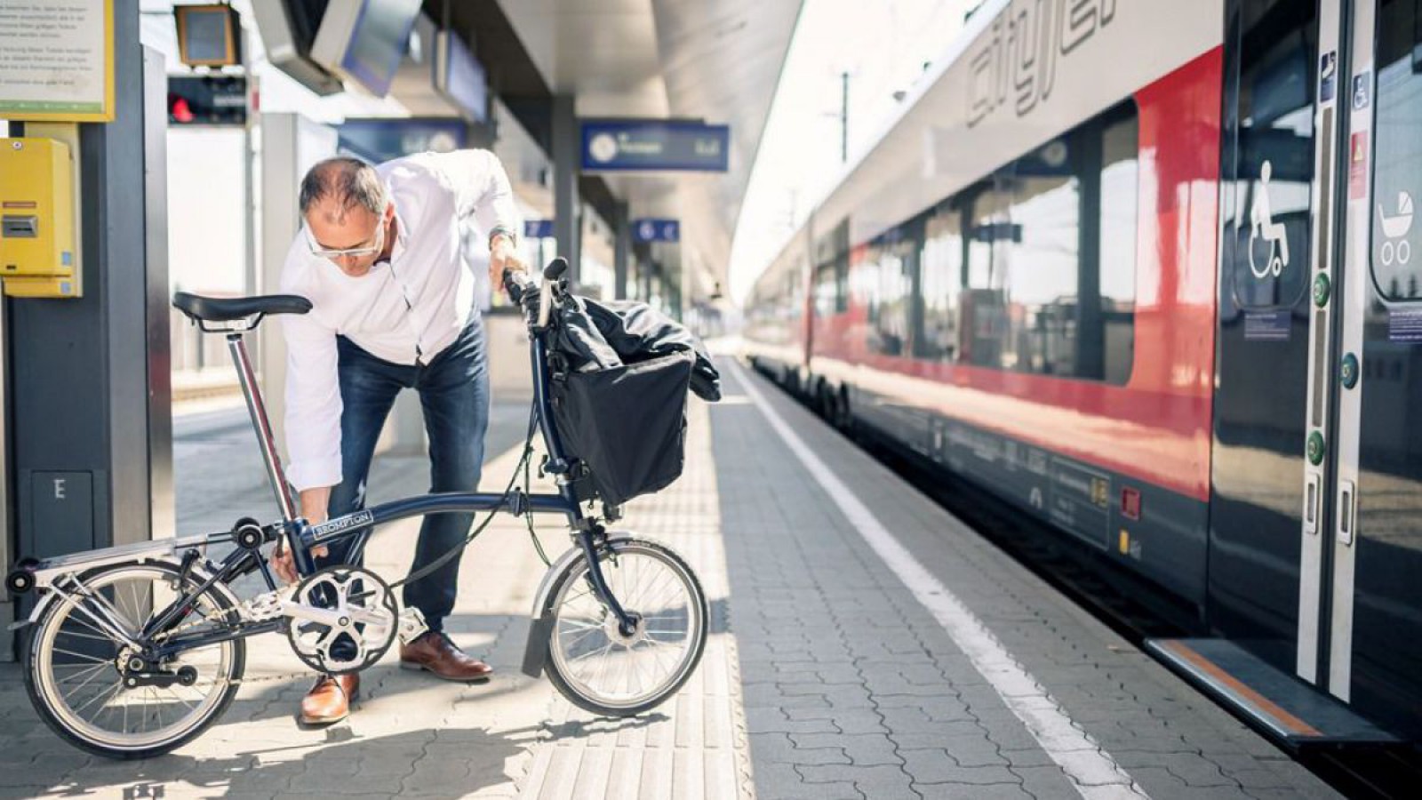 EIn Mann klappt sein Faltrad am Bahnhof zusammen um mit dem Zug weiter zu reisen.