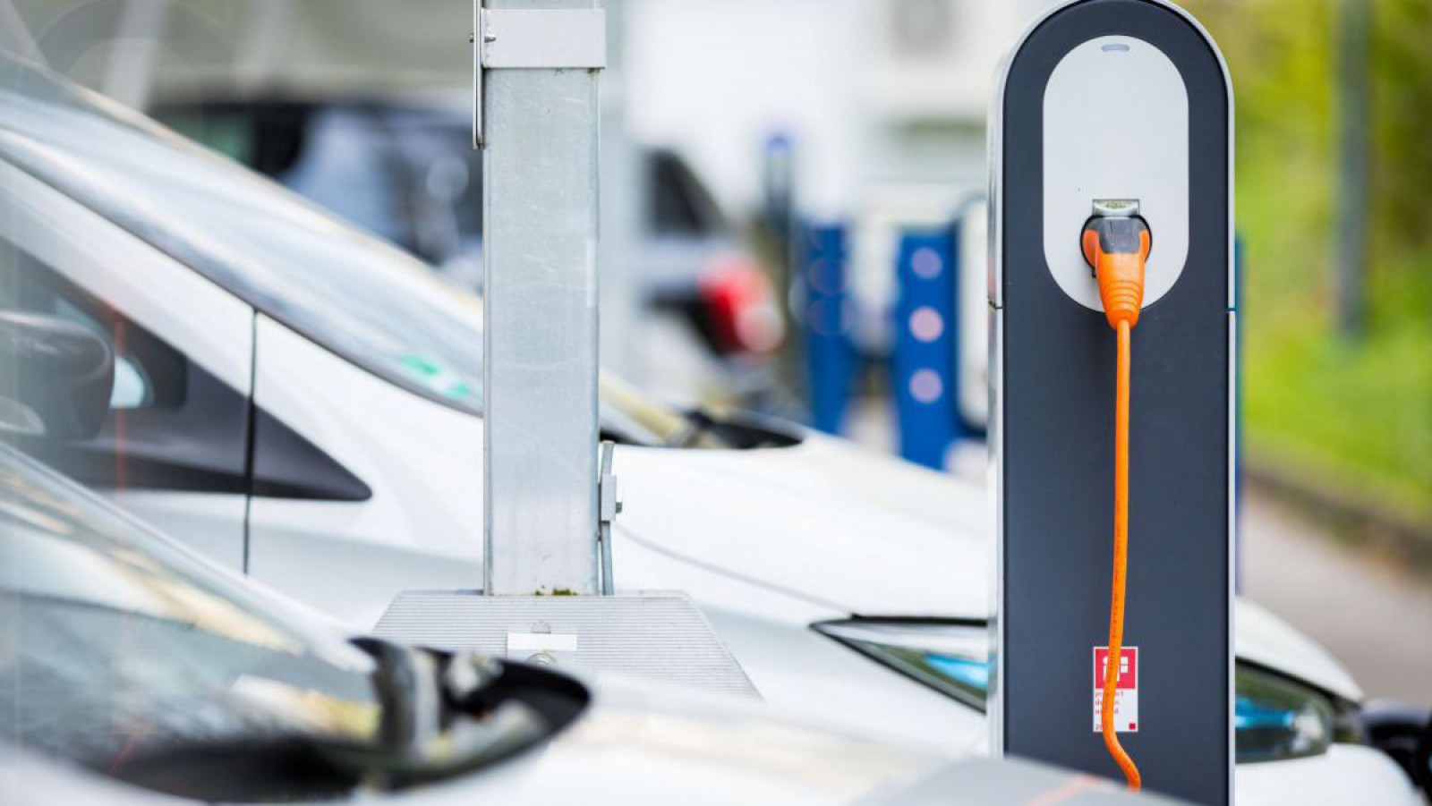 Stromtankstelle an der ein Elektroauto mit einem orangen Kabel geladen wird.