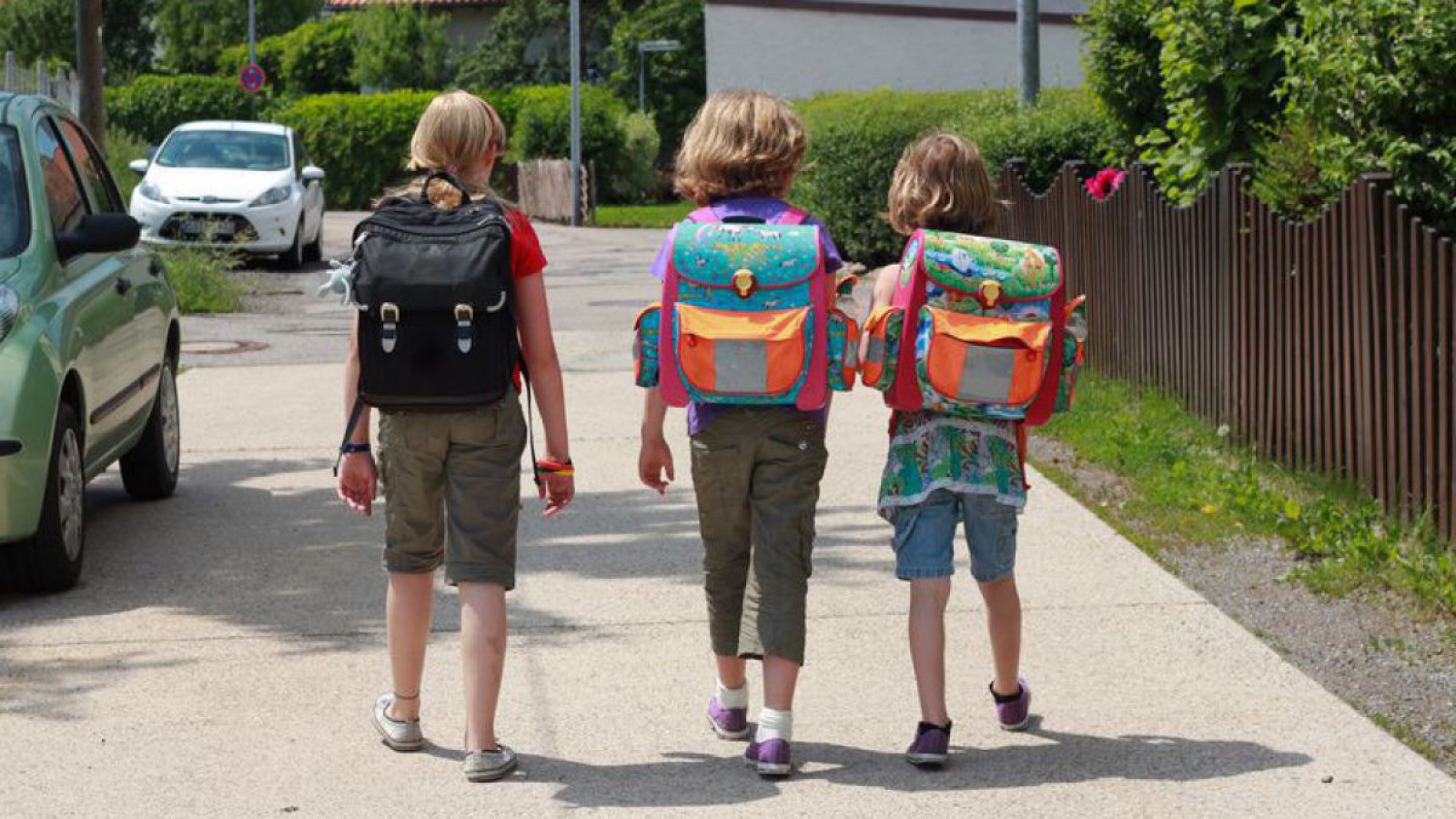Drei Kinder mit Schultaschen auf ihrem Schulweg