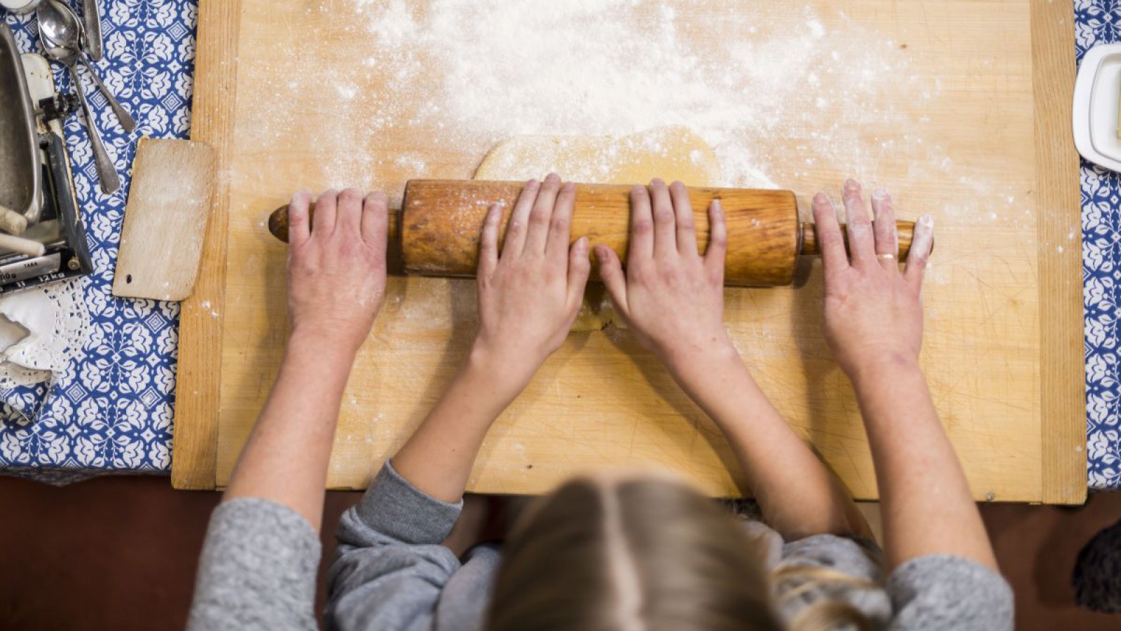 Eine Frau und ein Kind rollen gemeinsam einen Teig mit einer Teigrolle auf einem Holzbrett aus.