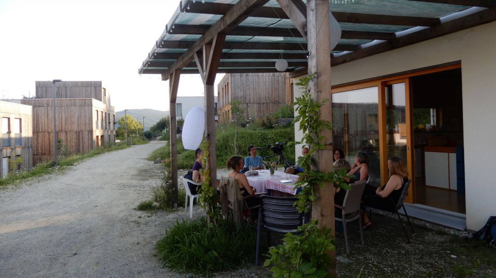 BewohnerInnen der Wohnhausanlage B.R.O.T. sitzen vor einem Haus an einem Tisch. 