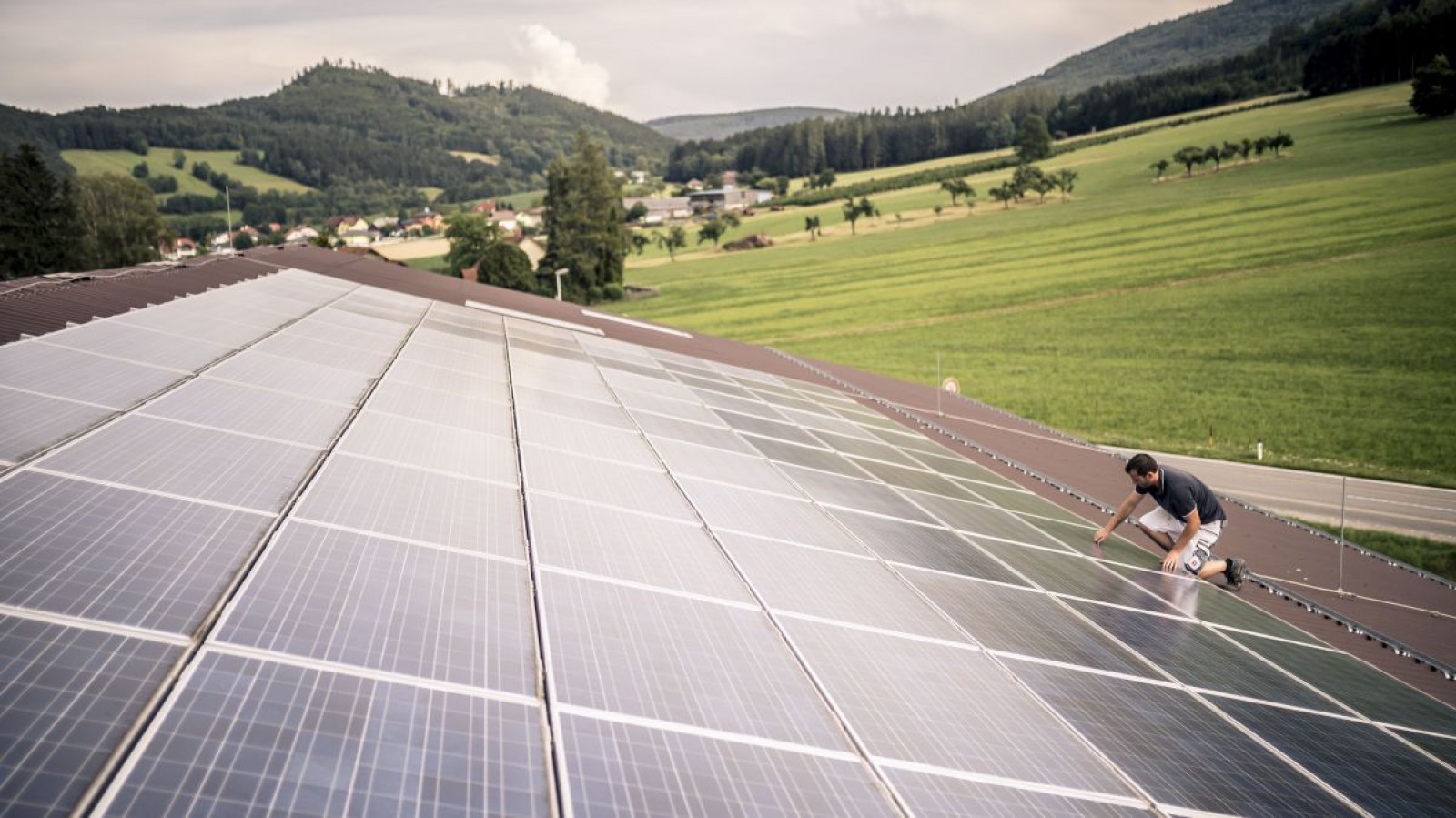 Ein Mann montiert Photovoltaikmodule auf das Dach eines landwirtschaftlichen Betriebes.