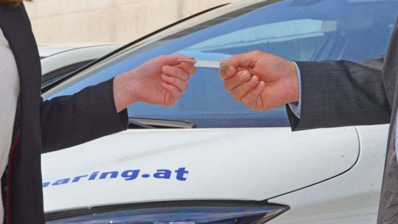 Eine Person übergibt eine Zugangskarte für ein Carsharing-Elektroauto an eine andere Person.