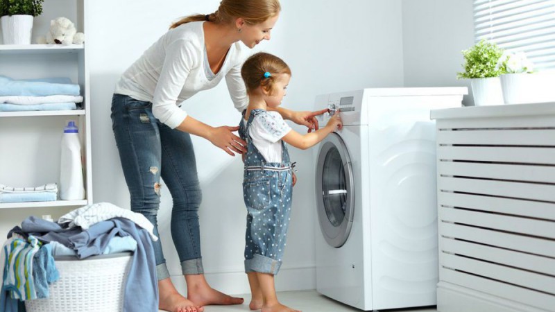 Frau und Kind schalten eine Waschmaschine ein