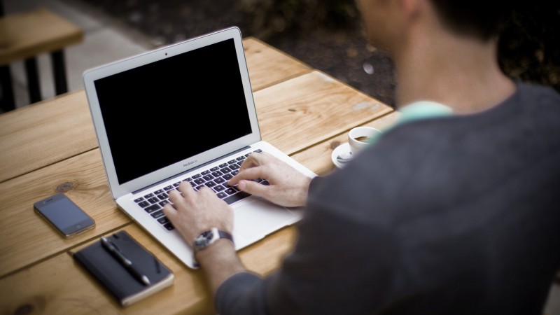 Mann mit Laptop sitzt an einem Holztisch